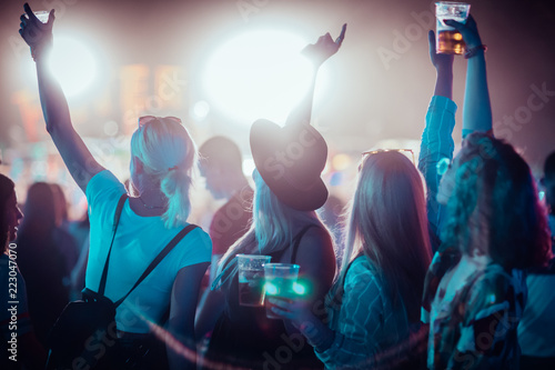 Back view of group of female friends at music festival drinking beer and dancing  photo