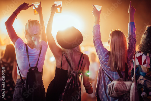 Back view of group of female friends at music festival drinking beer and dancing 