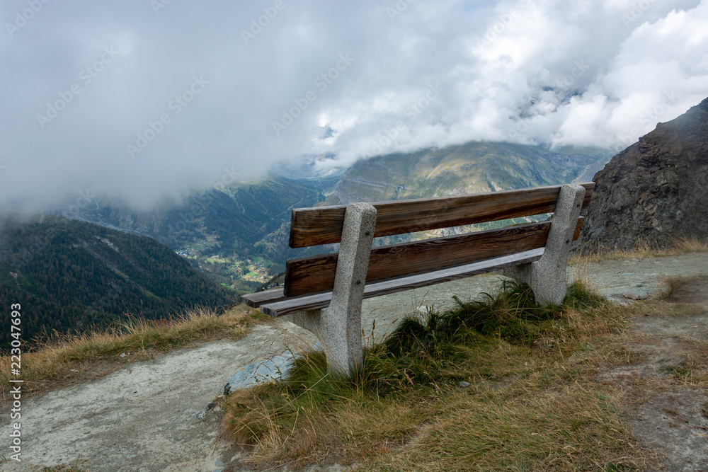 Wooden bench with beautiful mountain landscape with fog and clouds near the Matterhorn Wooden bench with beautiful mountain landscape with fog and clouds near the Matterhorn