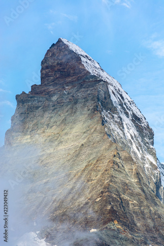 Peak of the Matterhorn with clouds swirling around and blue sky close up