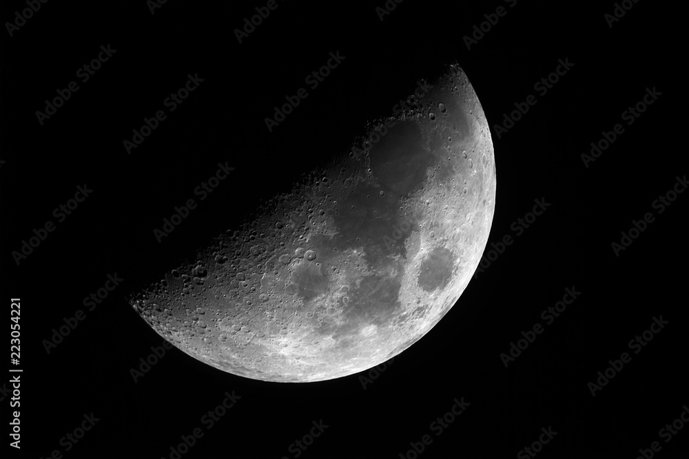 Naklejka premium Close up of bright Moon in first quarter phase with detailed craters in the shadow, taken with telescope, isolated in dark background.