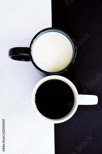 Two cups in front of a half black and half white background, one cup contains coffee, the other milk and both creat a contrast, concept for yin and yang with coffee cups