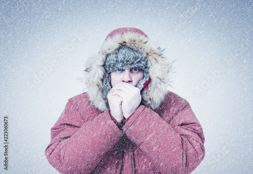 Frozen man in red winter clothes warming hands, cold, snow, frost, blizzard photo