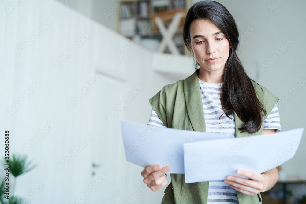 Portrait of brunette young woman holding two documents and reading them, copy space Portrait of brunette young woman holding two documents and reading them, copy space