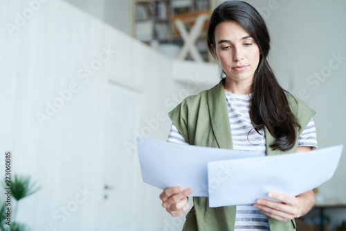 Portrait of brunette young woman holding two documents and reading them, copy space photo