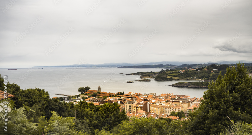 Fototapeta premium Vistas de Luanco en Asturias, España, pueblo mirando al mar en una panorámica con el colorido de los tejados, del mar y la vegetación, verano de 2018