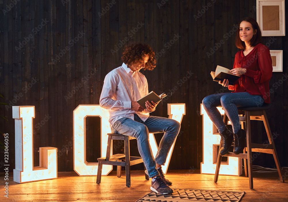 Young student couple reading together in a room decorated with voluminous letters with illumination. Young student couple reading together in a room decorated with voluminous letters with illumination.