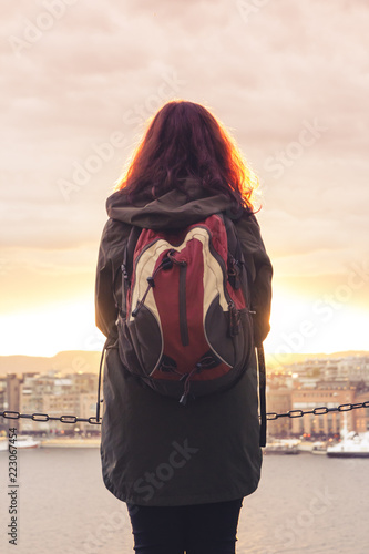 Canvas Print A lonely girl with a backpack stands with her back and looks at the beautiful pa