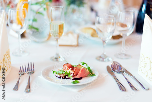 Prosciutto with parmesan cheese and rucola as a starter for wedding dish on the white table settings, light blurred background