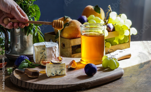 Delicious gourmet cheese Dorblu, honey, with sliced fresh figs and grapes, peaches, on a rustic wooden table
