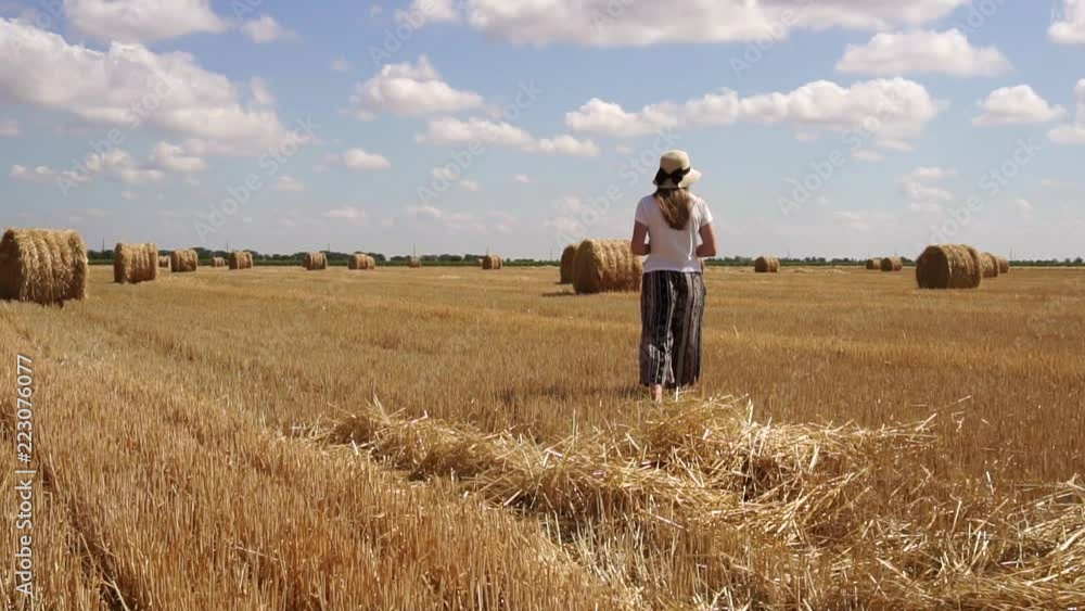 Calm relaxed young woman walking around fresh bale of hay organic wheat field in slow motion on hot summer landscape Calm relaxed young woman walking around fresh bale of hay organic wheat field in slow motion on hot summer landscape