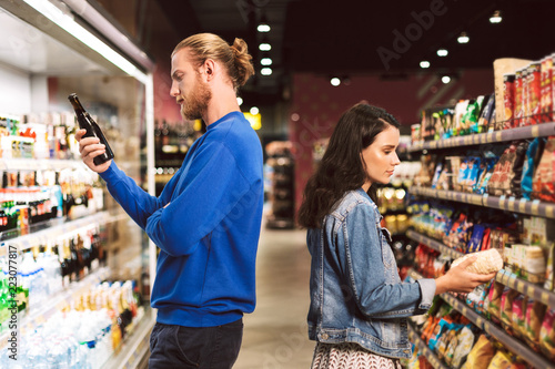 Young thoughtful couple standing back to back choosing products while spending time in modern supermarket