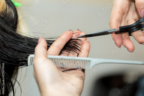 Closeup macro shot image of hairstylist hairdresser cutting customer woman hair in salon with scissors and comb, look from behind back side