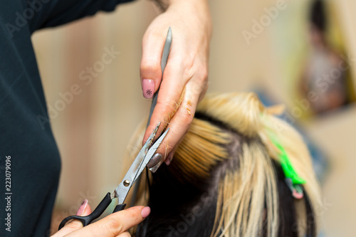 Closeup macro shot image of hairstylist hairdresser cutting customer woman hair in salon with scissors and comb, look from behind back side