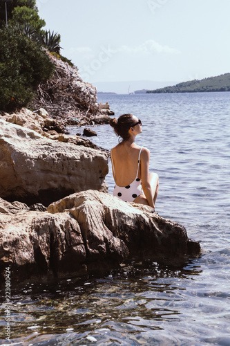 Young fashionable woman sitting and relaxing on a natural rocky coast, summer vacation concept