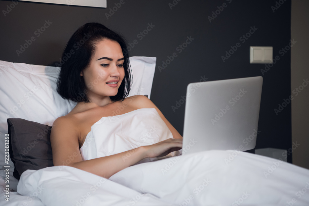 Woman working on laptop computer while lying on a bed at home. Woman working on laptop computer while lying on a bed at home.
