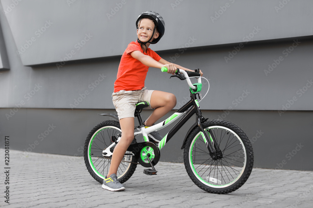 Little boy riding bicycle on street near gray wall Little boy riding bicycle on street near gray wall