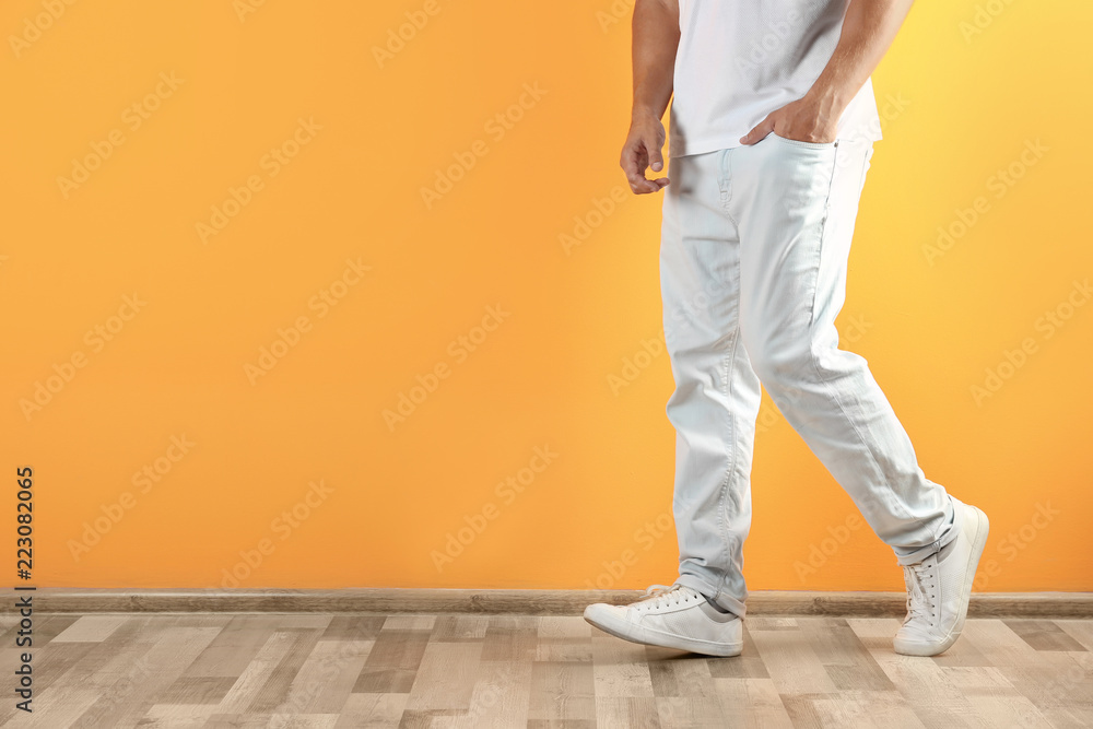 Young man in stylish jeans near color wall with space for text, focus on legs Young man in stylish jeans near color wall with space for text, focus on legs