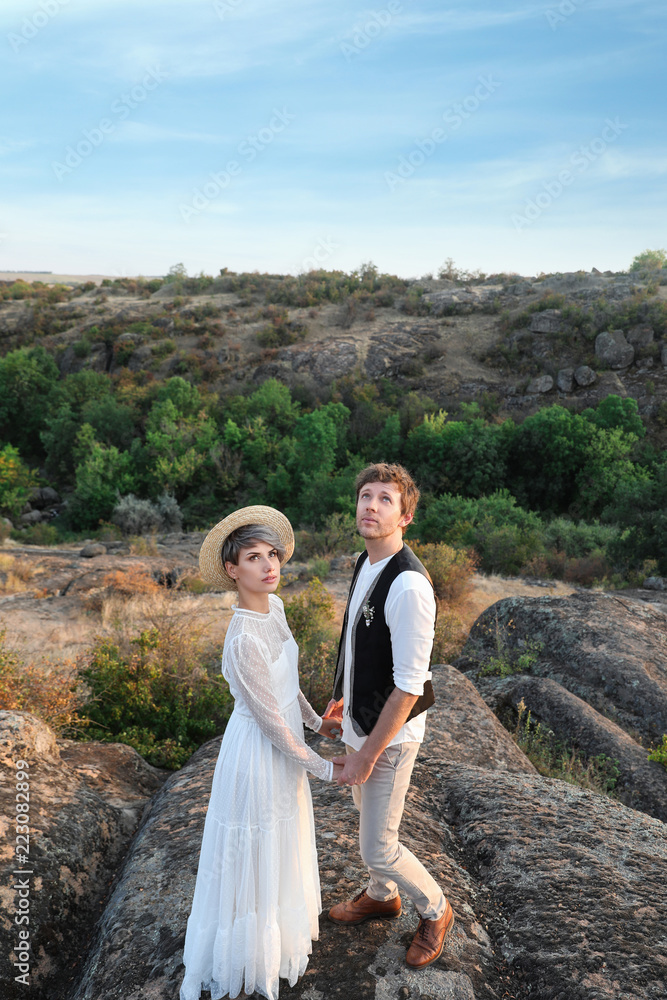 Happy newlyweds standing on rock outdoors