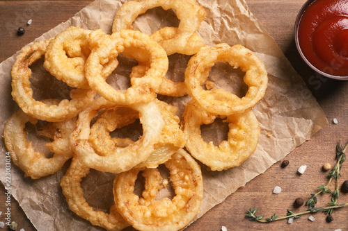 Homemade crunchy fried onion rings and sauce on wooden background, top view