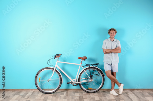 Handsome man with bicycle against color wall. Space for text