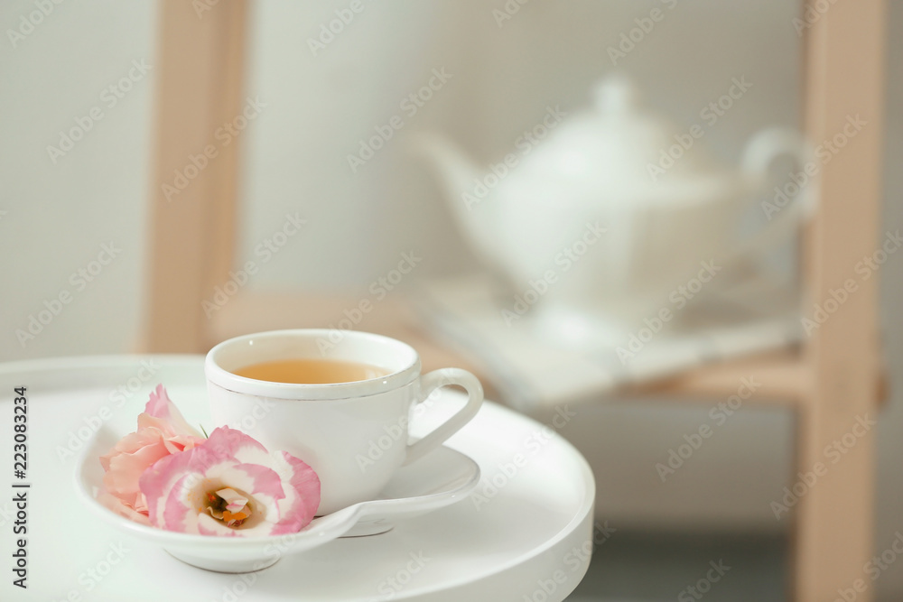 Cup of tea, saucer and flowers on table indoors Cup of tea, saucer and flowers on table indoors