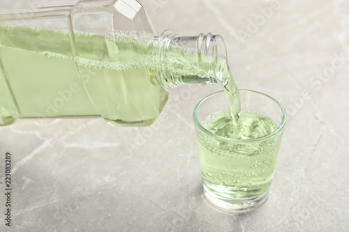 Pouring mouthwash in glass on light background. Teeth care