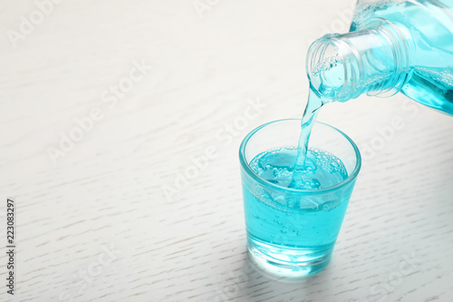Pouring mouthwash in glass and space for text on wooden background. Teeth care photo