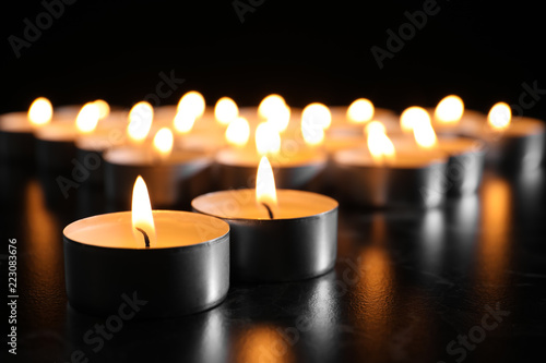 Burning candles on table in darkness, closeup. Funeral symbol
