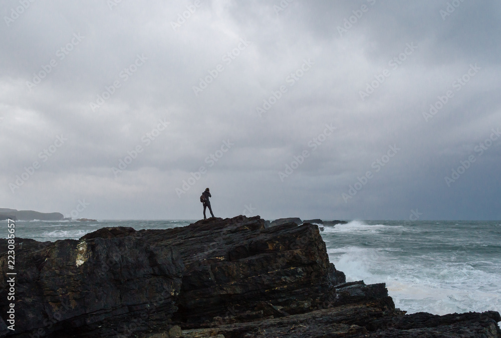 woman photographing on the edge of a cliff before a storm in the Cantabrian sea.