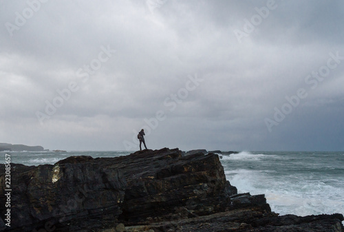 woman photographing on the edge of a cliff before a storm in the Cantabrian sea.