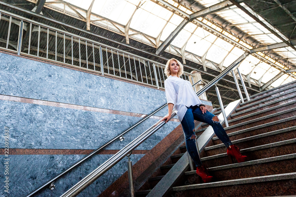 beautiful young girl in jeans and a white blouse elegantly stands on the stairs beautiful young girl in jeans and a white blouse elegantly stands on the stairs