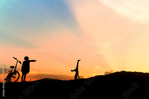 Happy children playing upside down outdoors in summer park walking on hands at sunset