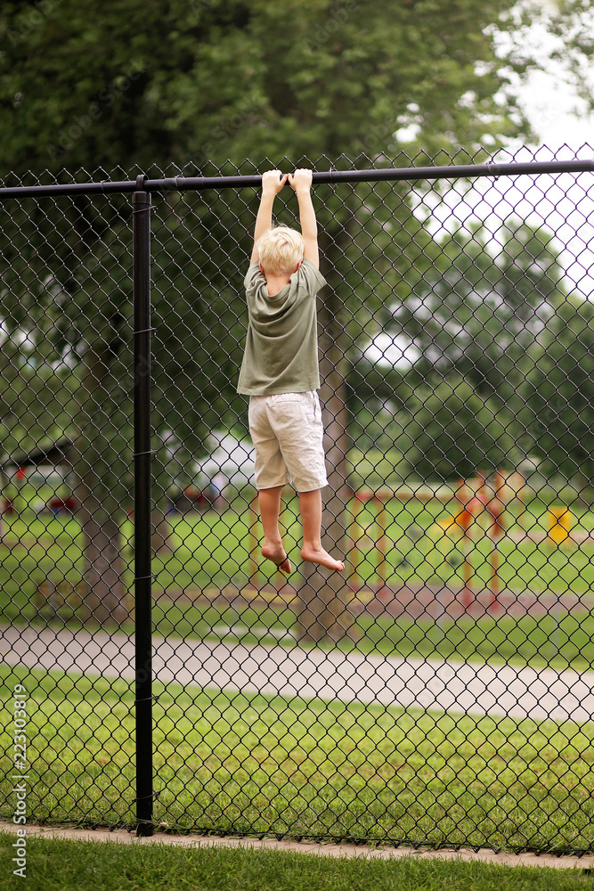 Little Boy Child Hanging From High Chain Link Fence Trying to Climb Out and Escape Little Boy Child Hanging From High Chain Link Fence Trying to Climb Out and Escape