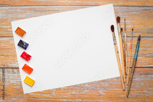 Flat lay of white Paper, watercolors, paint brush on brown wooden table