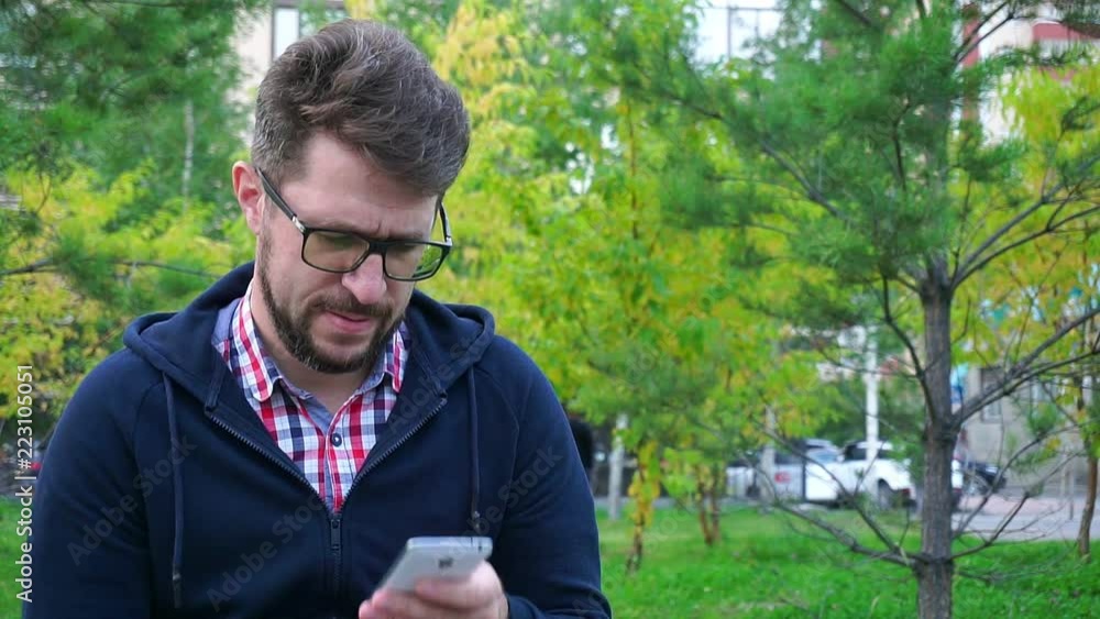 Angry man with a beard sitting in the Park. Writes messages in phone Angry man with a beard sitting in the Park. Writes messages in phone