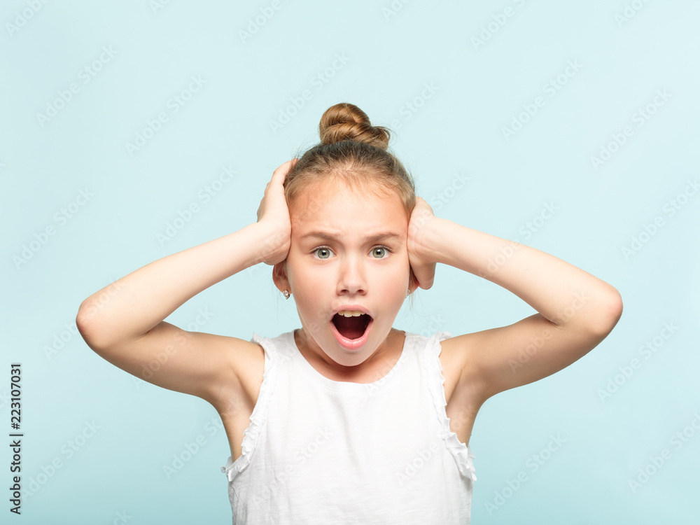 omg unbelievable shock amazement. dumbfounded child clutching her head with hands. portrait of a young girl on blue background. emotion facial expression and reaction concept. omg unbelievable shock amazement. dumbfounded child clutching her head with hands. portrait of a young girl on blue background. emotion facial expression and reaction concept.