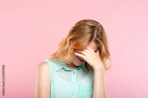 facepalm embarrassment and shame emotion. ashamed smiling girl covering her face with a hand. young beautiful woman portrait on pink background. photo
