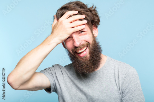 facepalm. happy smiling joyful man covering his face. shame and embarrassment concept. portrait of a young bearded guy on blue background. emotion facial expression.