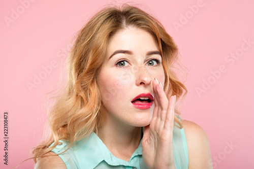 amazed shocked girl telling a secret or spreading rumor and gossipping. sharing information concept. young beautiful female portrait on pink background.