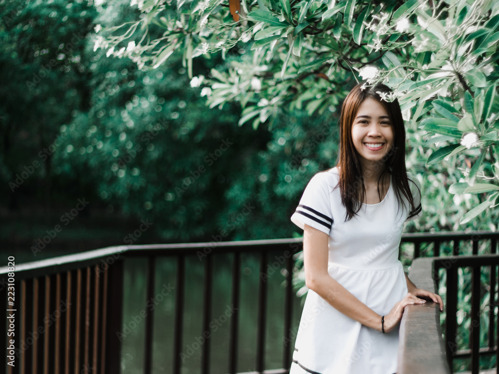 The girl wearing white dress and she is standing on the red wood bridge with tree and canal background , style dark green tone, bang krachao island in samut prakan at Thailand The girl wearing white dress and she is standing on the red wood bridge with tree and canal background , style dark green tone, bang krachao island in samut prakan at Thailand
