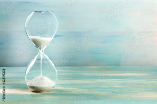 Obraz na plátně A side view of an hourglass with falling sand, on a teal background with copy sp