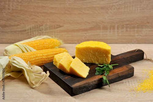 Corn hominy sliced into slices on a wooden board. Two cobs of ripe corn. Light background. Close-up.  photo