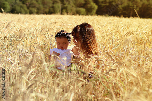 Happy mother holding baby girl on a wheat field in sunlight. Family happiness concept.