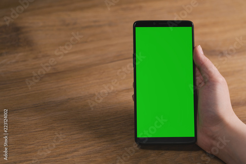 young female hand holding smartphone with big screen on wood oak table with copy space