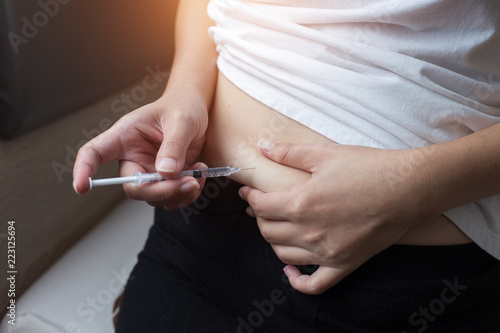 Woman with syringe inject insulin to her belly - diabetes concept