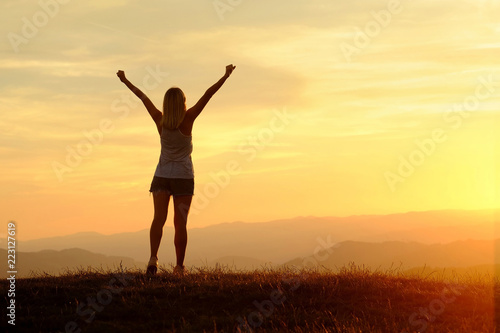 Happy woman with open arms stay on the peak of the mountain clif