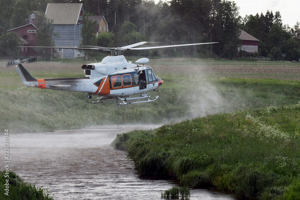 Fototapeta premium Fire fighting helicopter filling a water bucket from a small river to extinguish the forest fire.