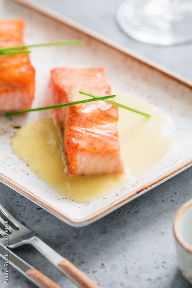 The beautiful serving of cooked fried salmon steak on a ceramic plate at a restaurant. The beautiful serving of cooked fried salmon steak on a ceramic plate at a restaurant.