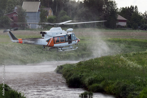 Fire fighting helicopter filling a water bucket from a small river to extinguish the forest fire.